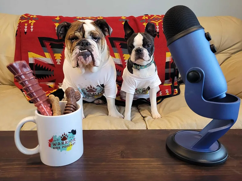 Ernie & Peter sitting on a couch. In front of them is a mug full of treats and a microphone.